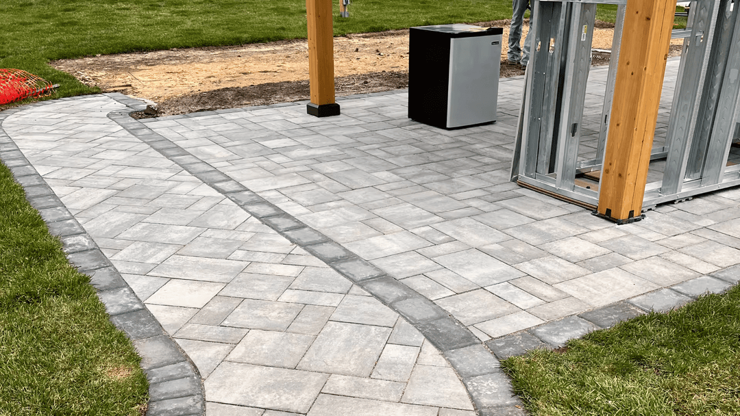 Paved pathway and patio area with gray stone, surrounded by grass and construction site.