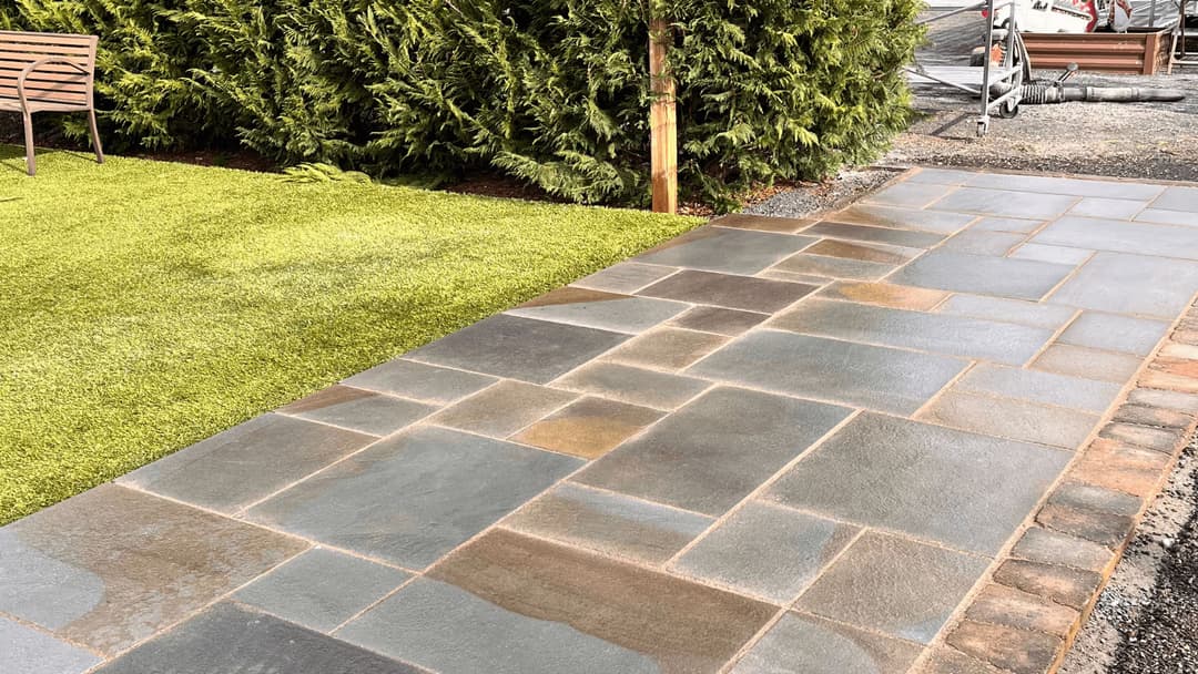 Stone pathway leading to manicured grass and shrubs in a landscaped garden.
