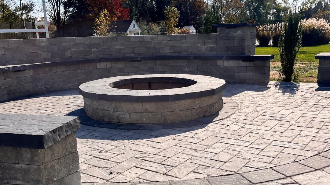 Stone outdoor fire pit surrounded by a circular seating wall in a landscaped yard.