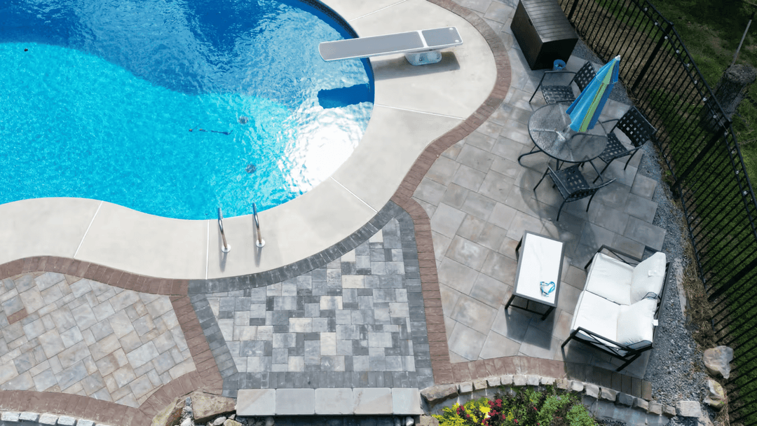 Aerial view of a swimming pool with a patio area, lounge chairs, and landscaping.