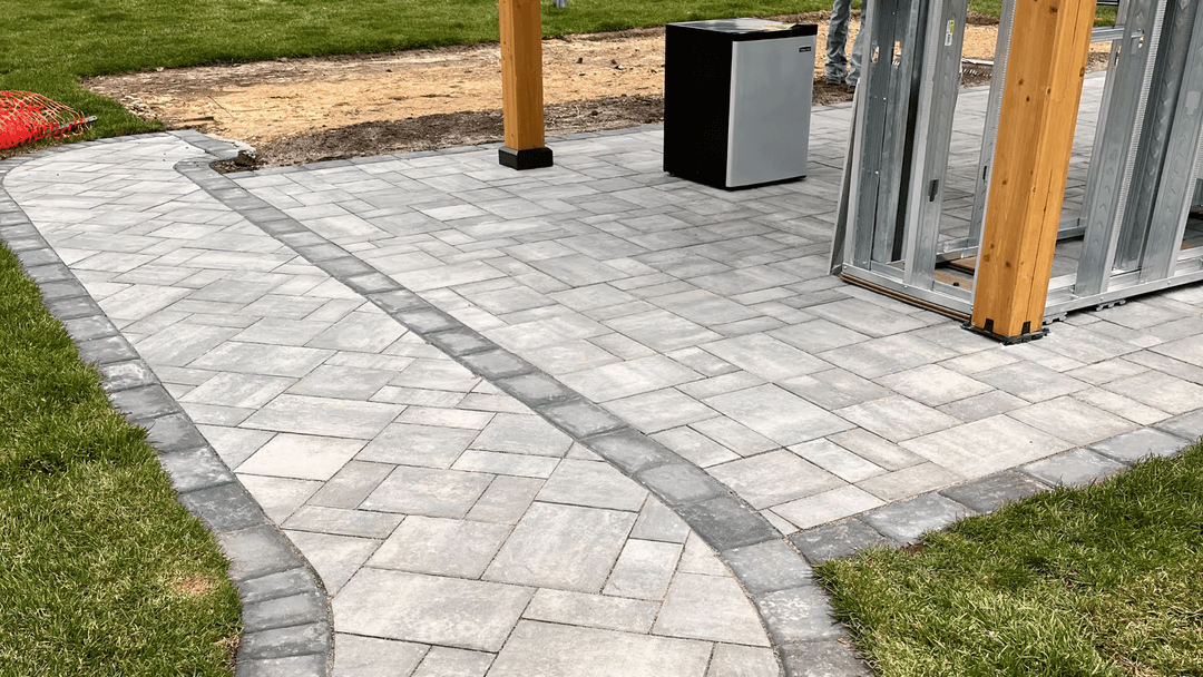 Paved walkway with gray stones leading to a garden shed and trash can on green grass.