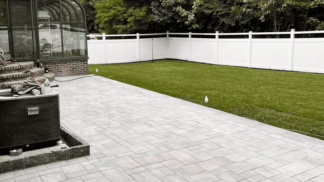 Patio renovation with pavers and green lawn, fenced yard, and air conditioning unit.