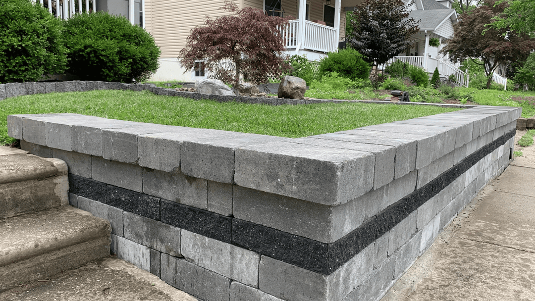 Gray and black stone retaining wall with green grass and landscaped yard in background.