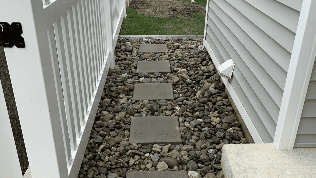 Stone pathway with concrete stepping stones and pebbles between two fences.