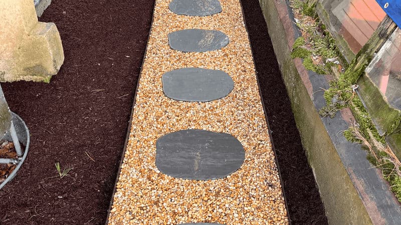 Garden pathway with slate stepping stones over gravel and dark mulch borders.