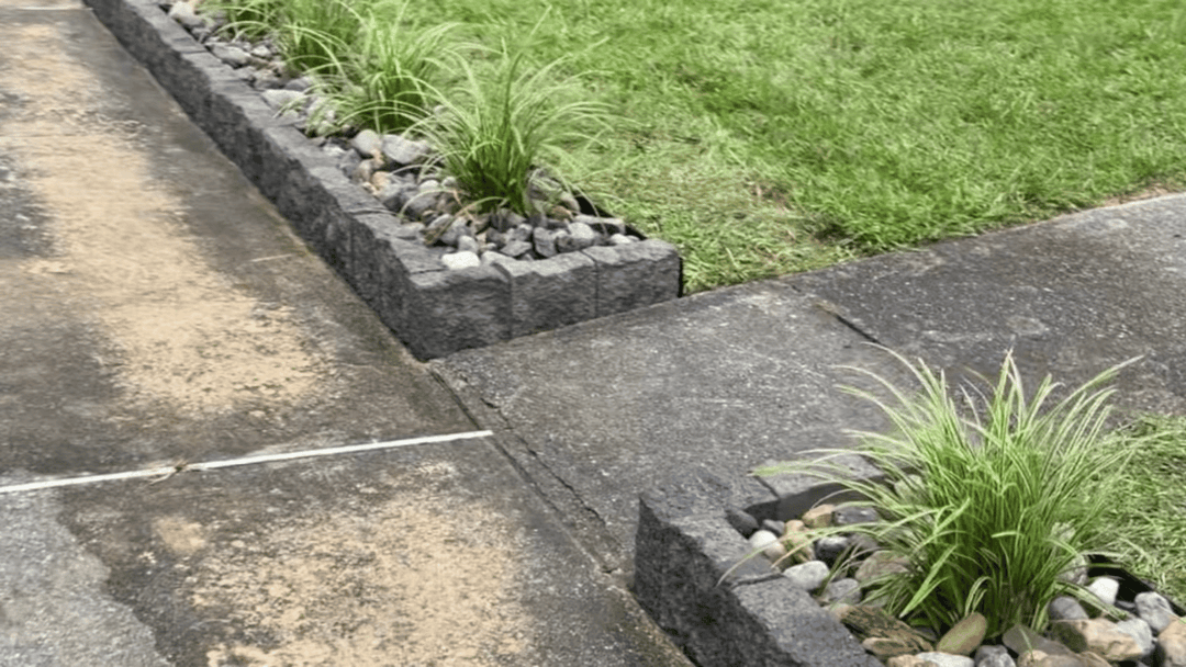 Decorative stone planters with ornamental grasses lining a concrete pathway.
