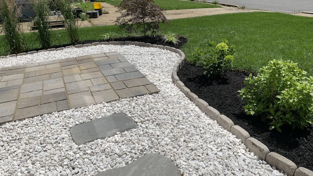 Landscaped yard featuring white gravel, stone walkway, and lush green grass.