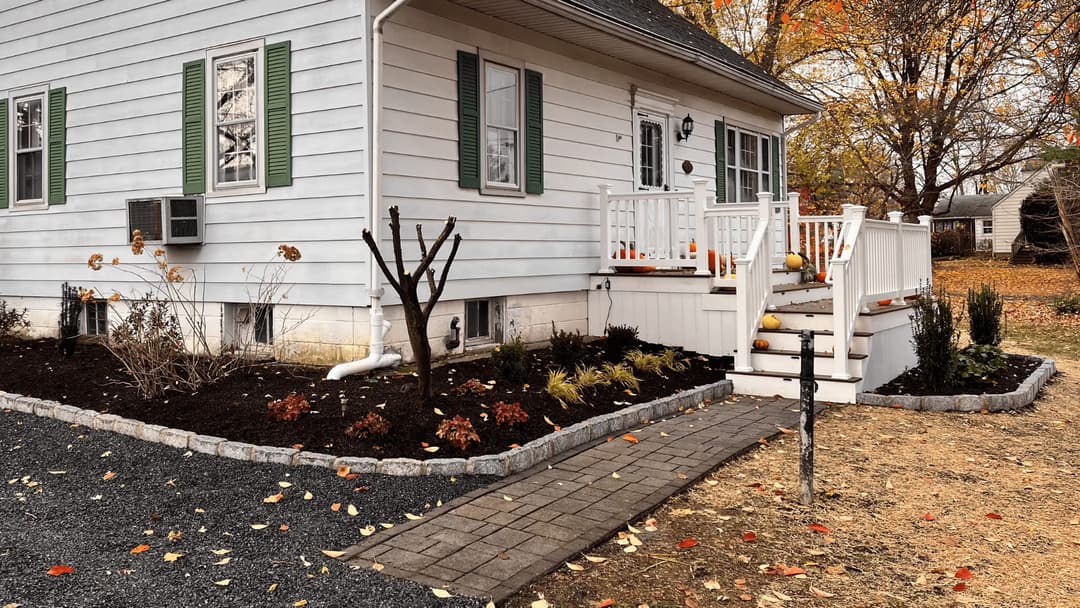 Cozy white house with green shutters, autumn landscaping, and a welcoming front porch.