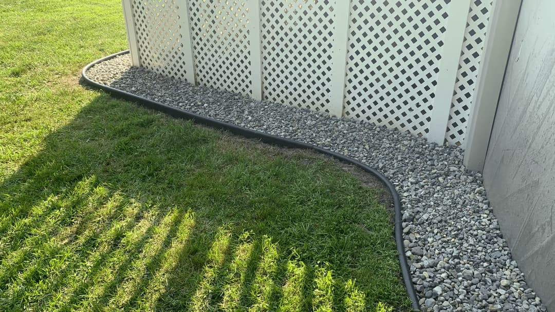 Curved gravel landscaping along a white lattice fence in a sunny yard.