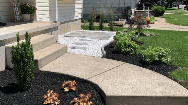 landscaped front yard with curved walkway, stone path, and vibrant green plants.