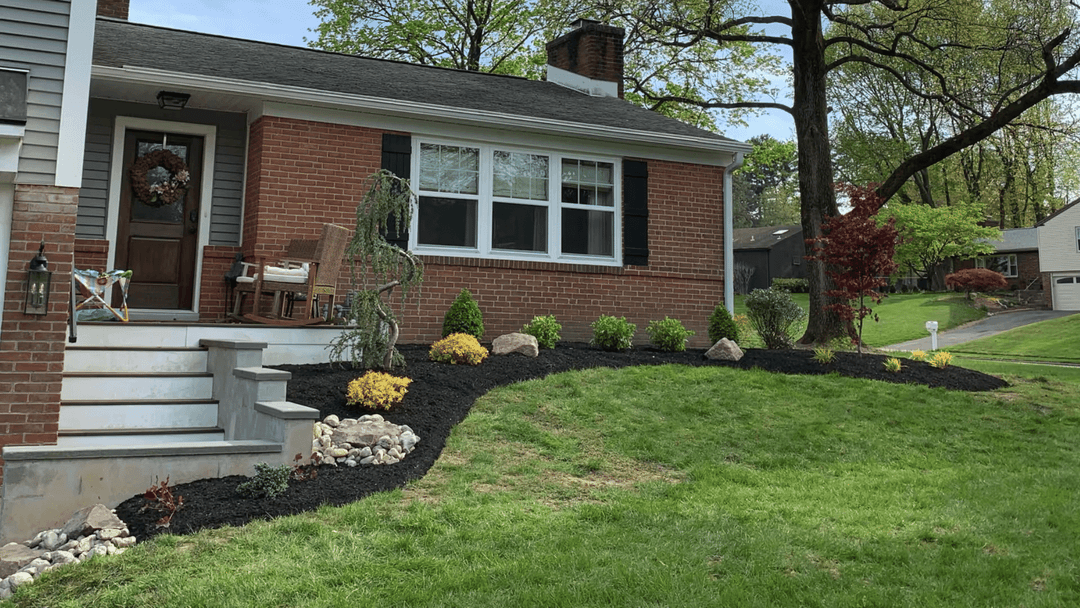 Renovated front yard with landscaped border, shrubs, and rocks alongside a brick home.