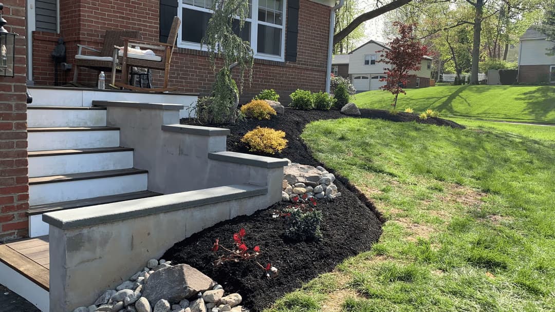 Front yard landscaping with stone steps, colorful shrubs, and mulch near a brick home.