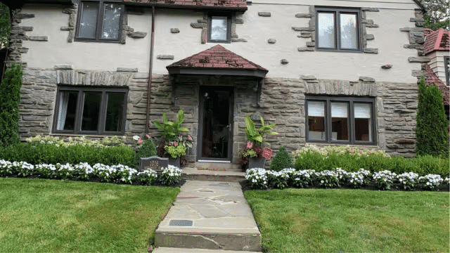 Charming stone-front house with landscaped garden and pathway, featuring white flowers.