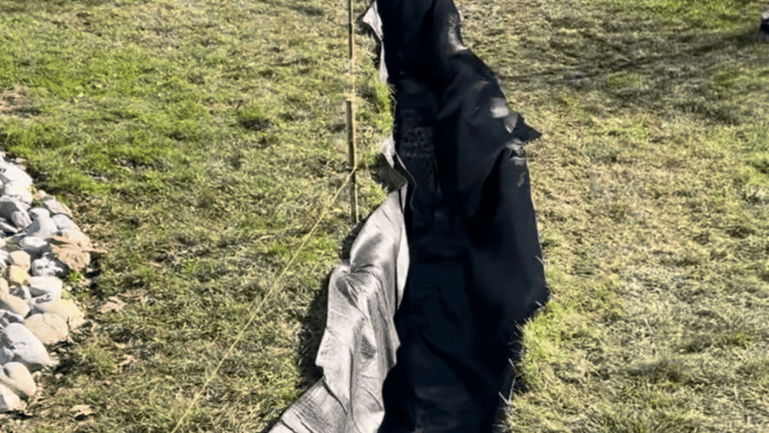 Black landscape fabric laid in a trench on grass, ready for garden landscaping.