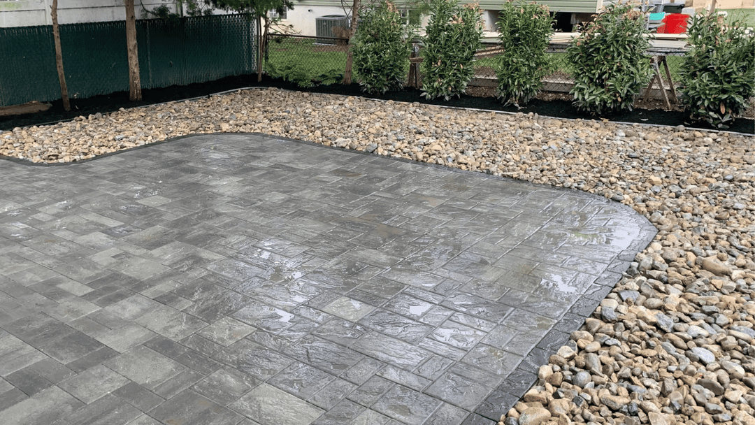 Paved patio with gray tiles, surrounded by decorative stones and greenery.