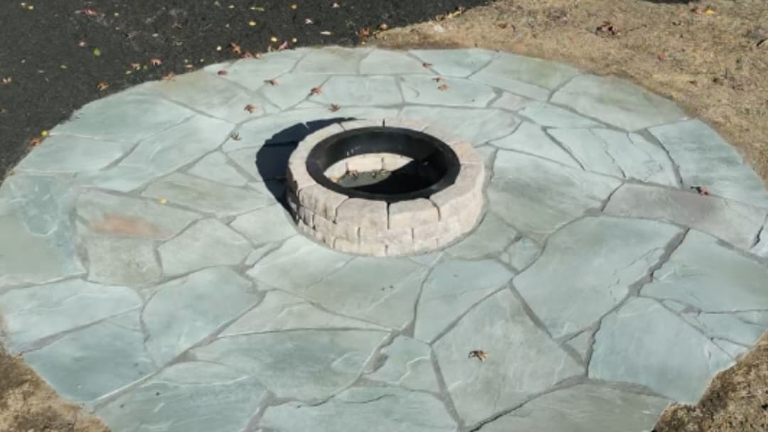 Circular stone fire pit surrounded by a slate stone patio in a grassy area.