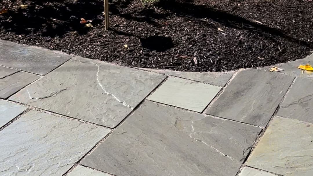 Natural stone patio with gray slate tiles and dark mulch border in landscaped garden.