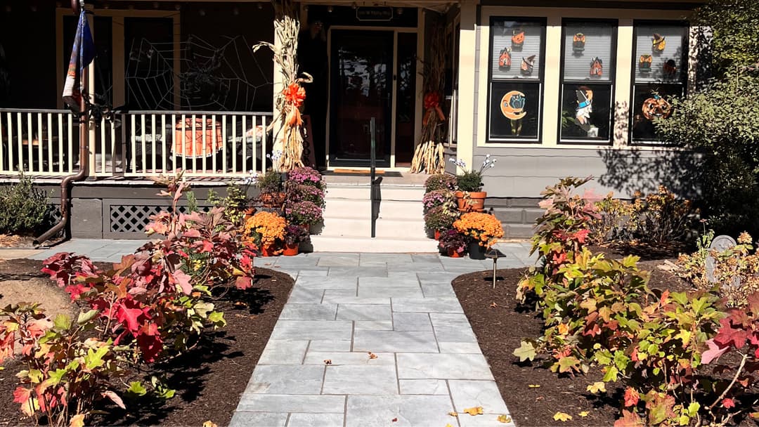 Colorful autumn garden pathway leading to a decorated porch with seasonal decorations.