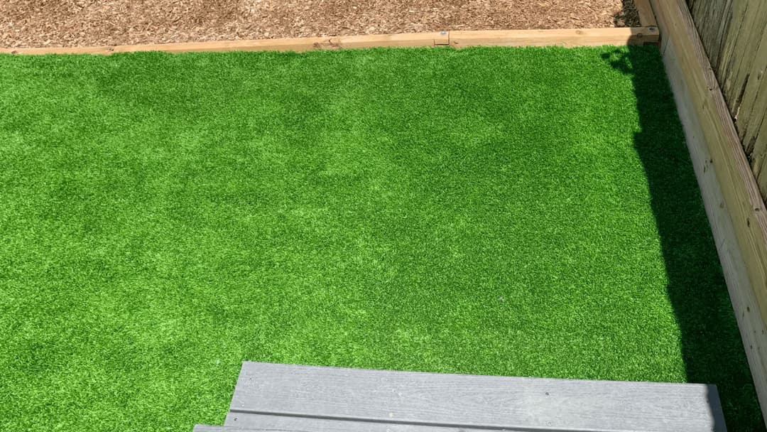 Lush green artificial turf yard with wooden steps and a mulch border.
