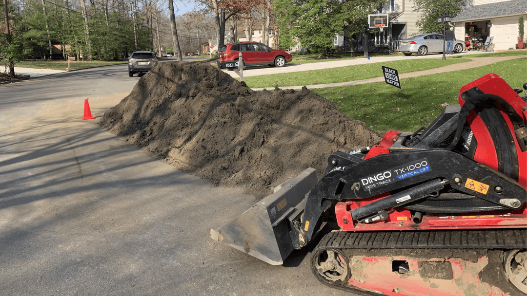 Dingo TX1000 compact track loader beside a large dirt pile on a residential street.