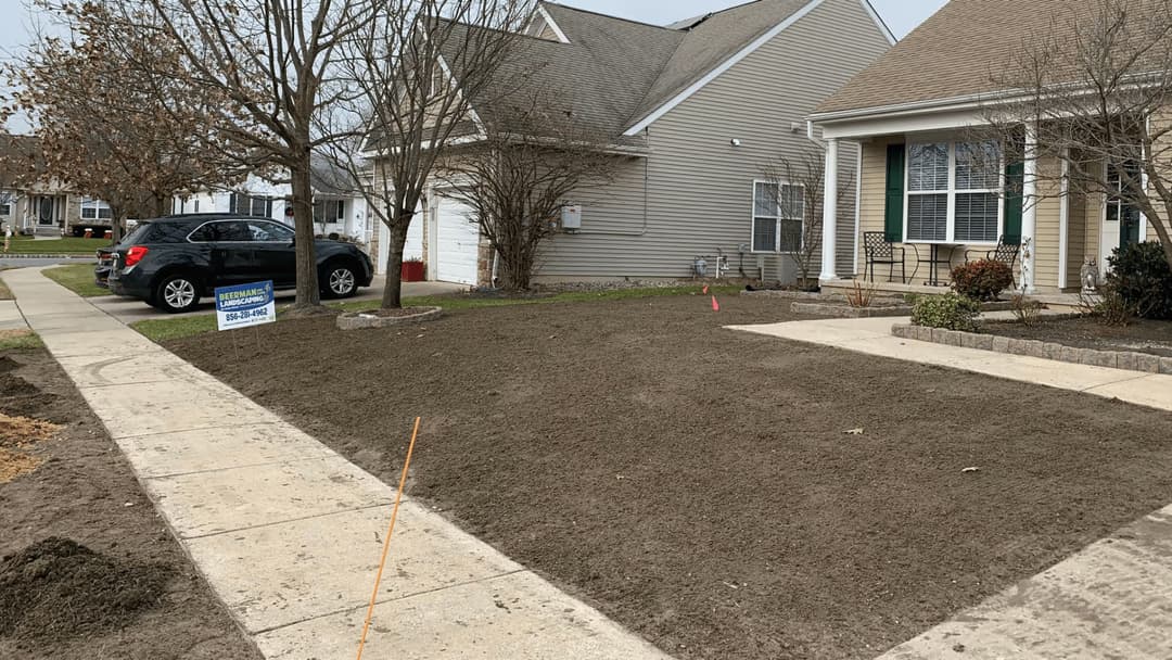 Landscaped front yard with fresh dirt, driveway, and renovation sign in residential area.