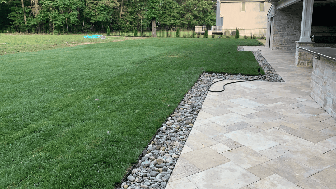 Lush green lawn beside a patio with stone borders and natural landscaping.