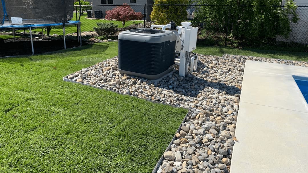 Swimming pool area featuring a heat pump surrounded by decorative rocks and lush green grass.