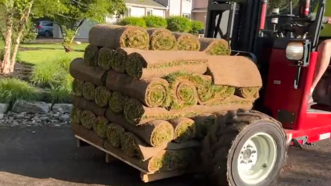 Pallet of rolled sod being transported by tractor in residential landscaping project.