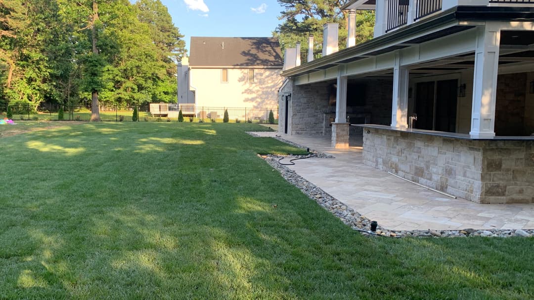 Well-maintained backyard with stone patio, green lawn, and modern house exterior in the background.