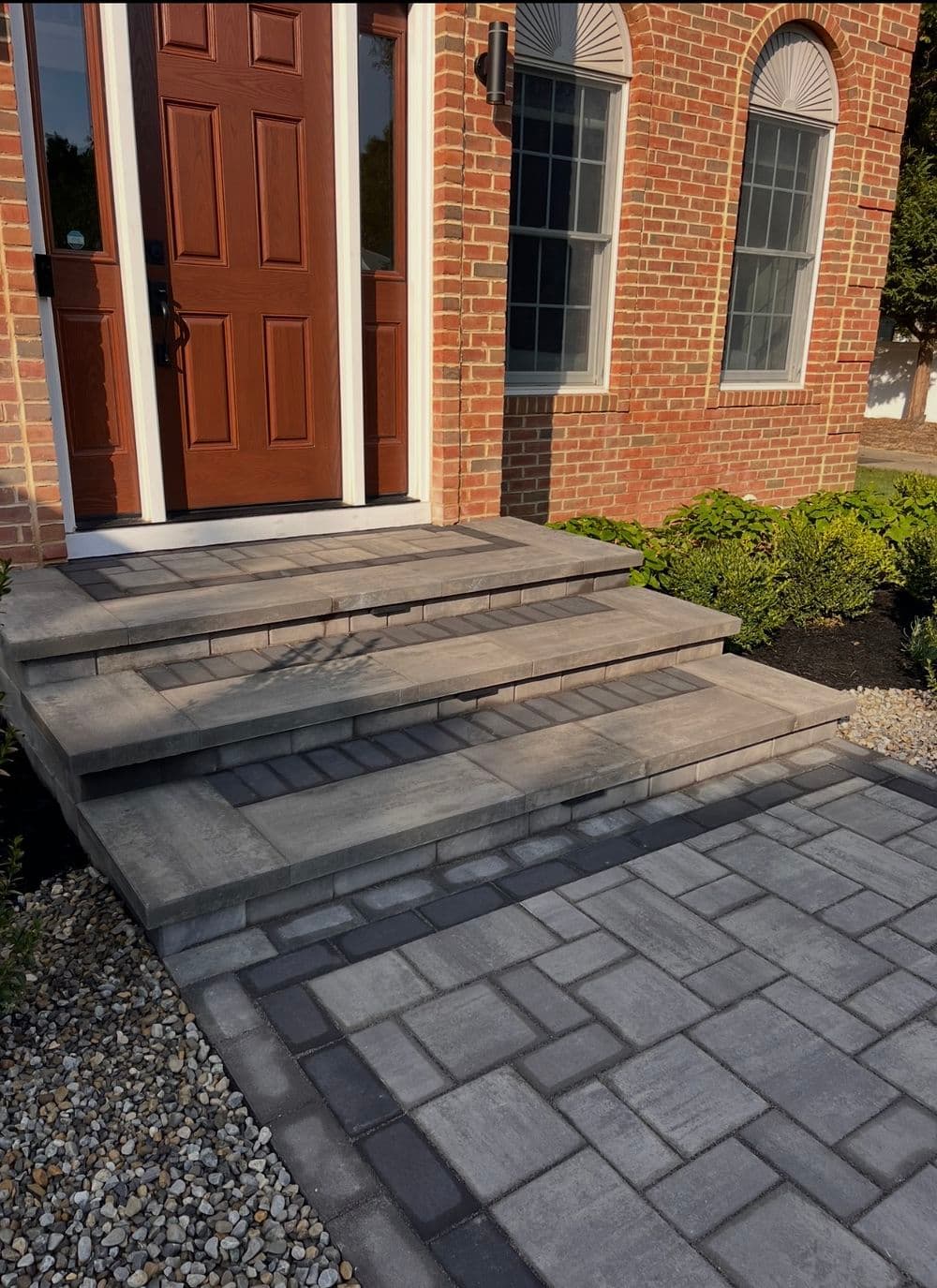 Newly installed paver stone steps leading to a brick home entrance with landscaped surroundings.