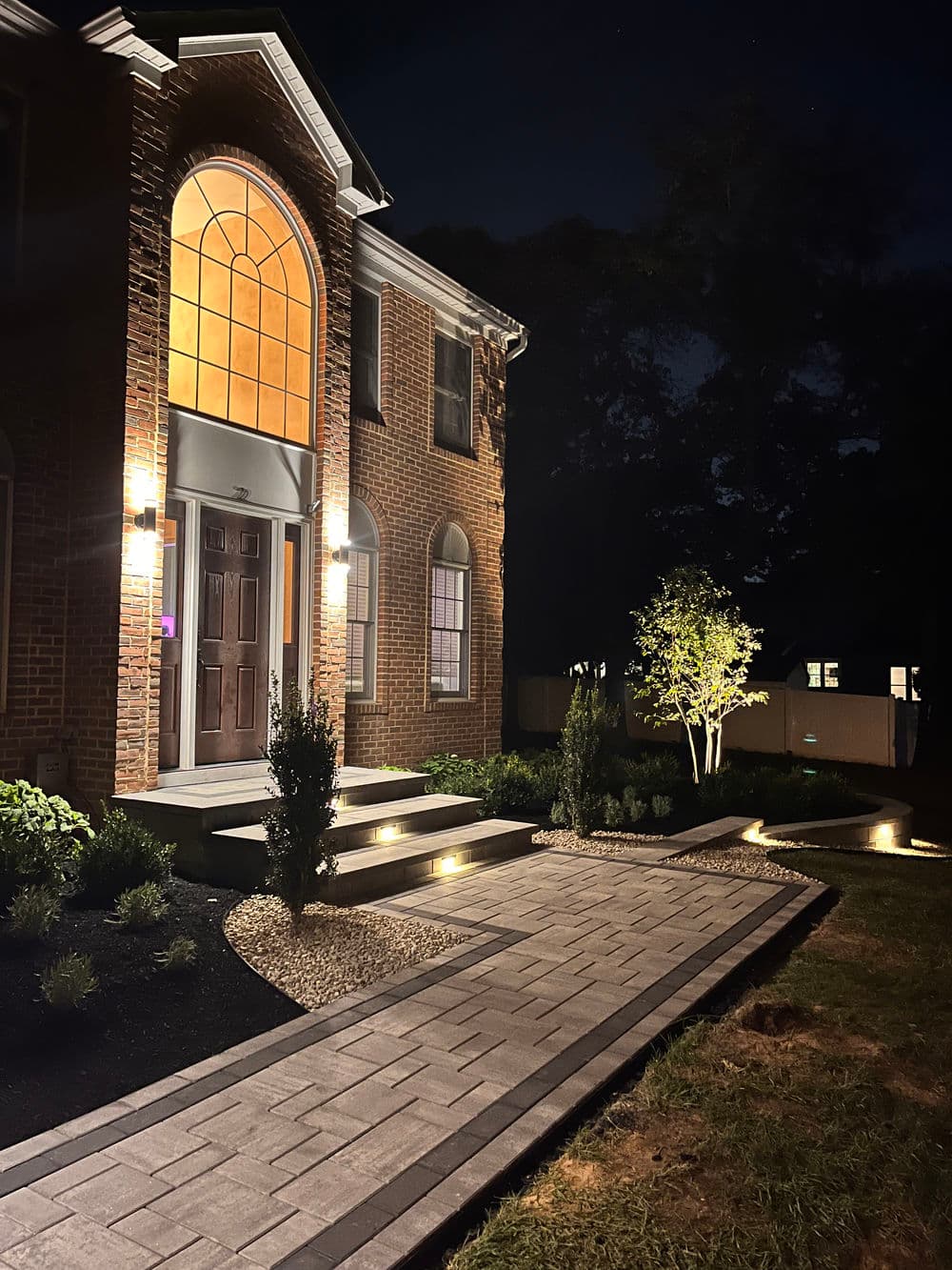 Elegant brick home exterior at night with illuminated walkway and landscaped garden.