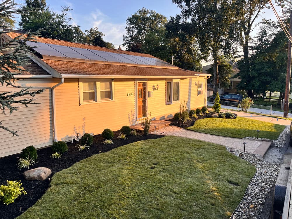 Modern home with solar panels, well-manicured lawn, and landscaped garden. Bright afternoon light.