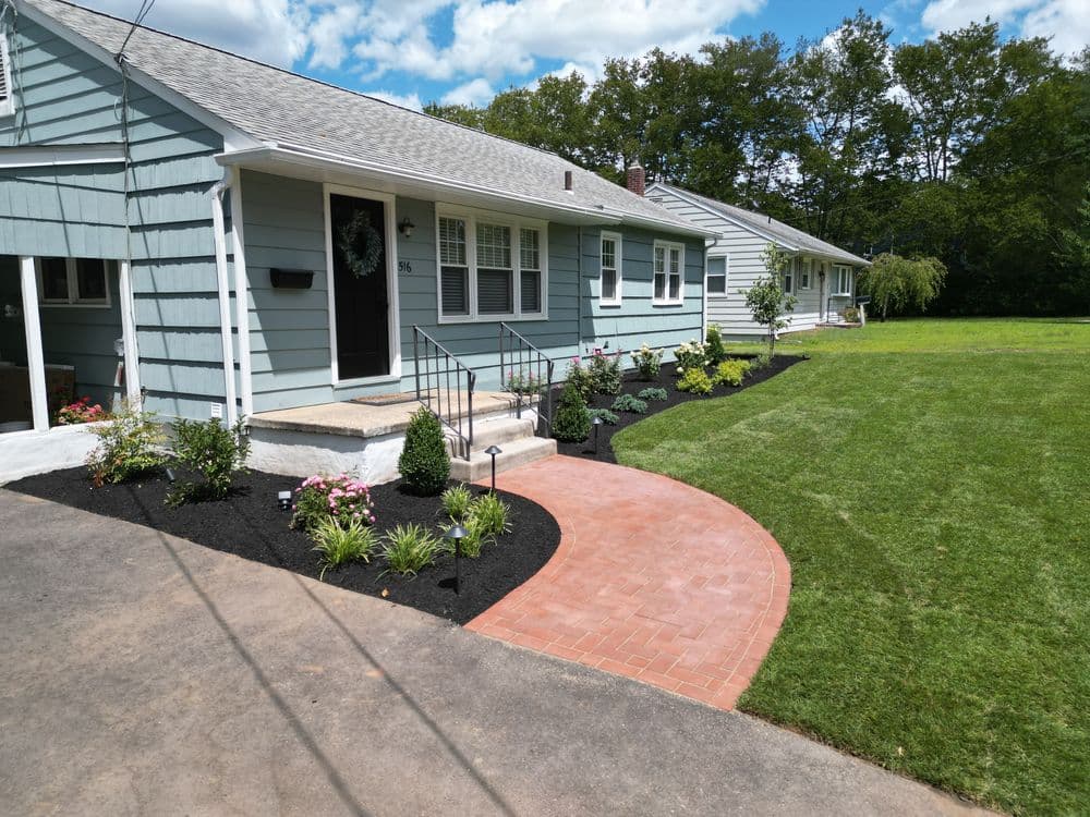 Charming blue house with a landscaped path and garden, featuring green lawn and flowers.