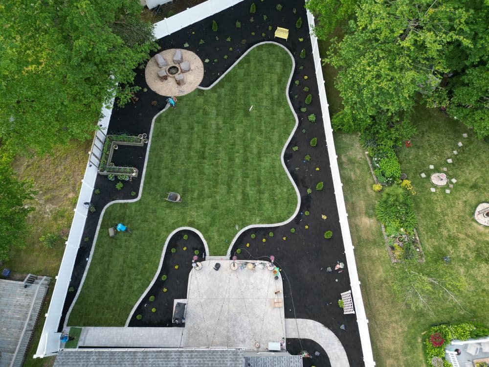 Aerial view of a landscaped backyard with a black mulch garden, lawn, and seating area.