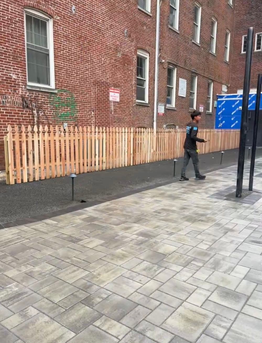 Person walking past a newly constructed wooden fence beside a brick building.