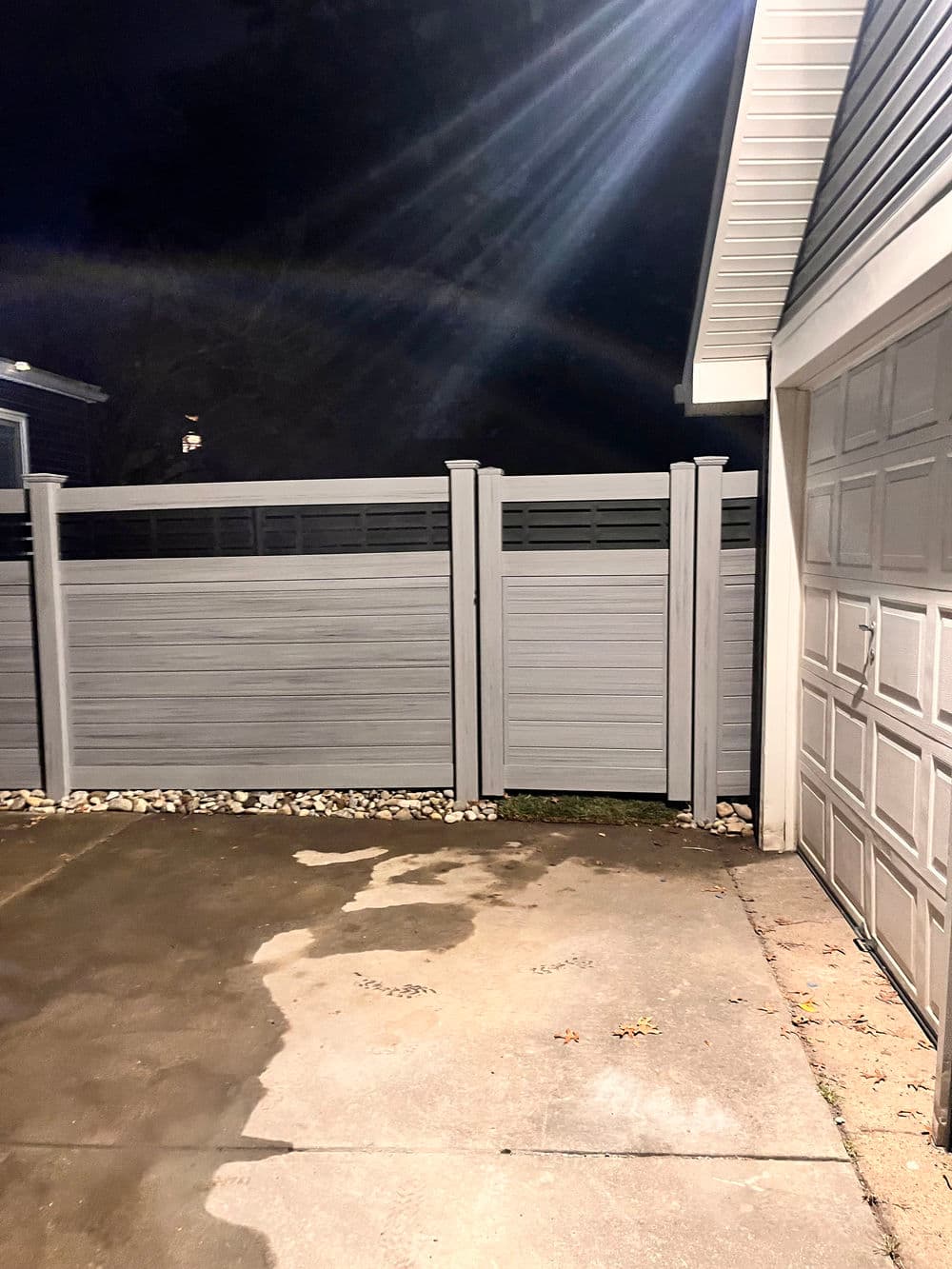Modern gray privacy fence with decorative panels beside a driveway at night.